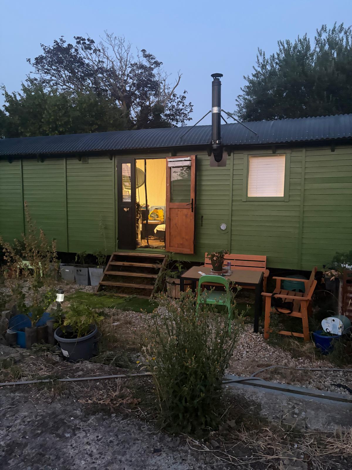Large green shepherd’s hut glowing from within at dusk