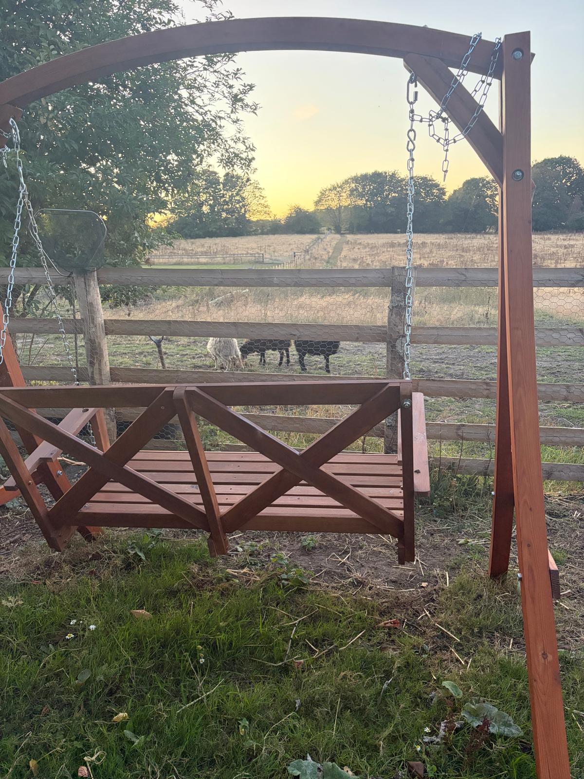 Wooden swing looking over the paddock and sheep at sunset