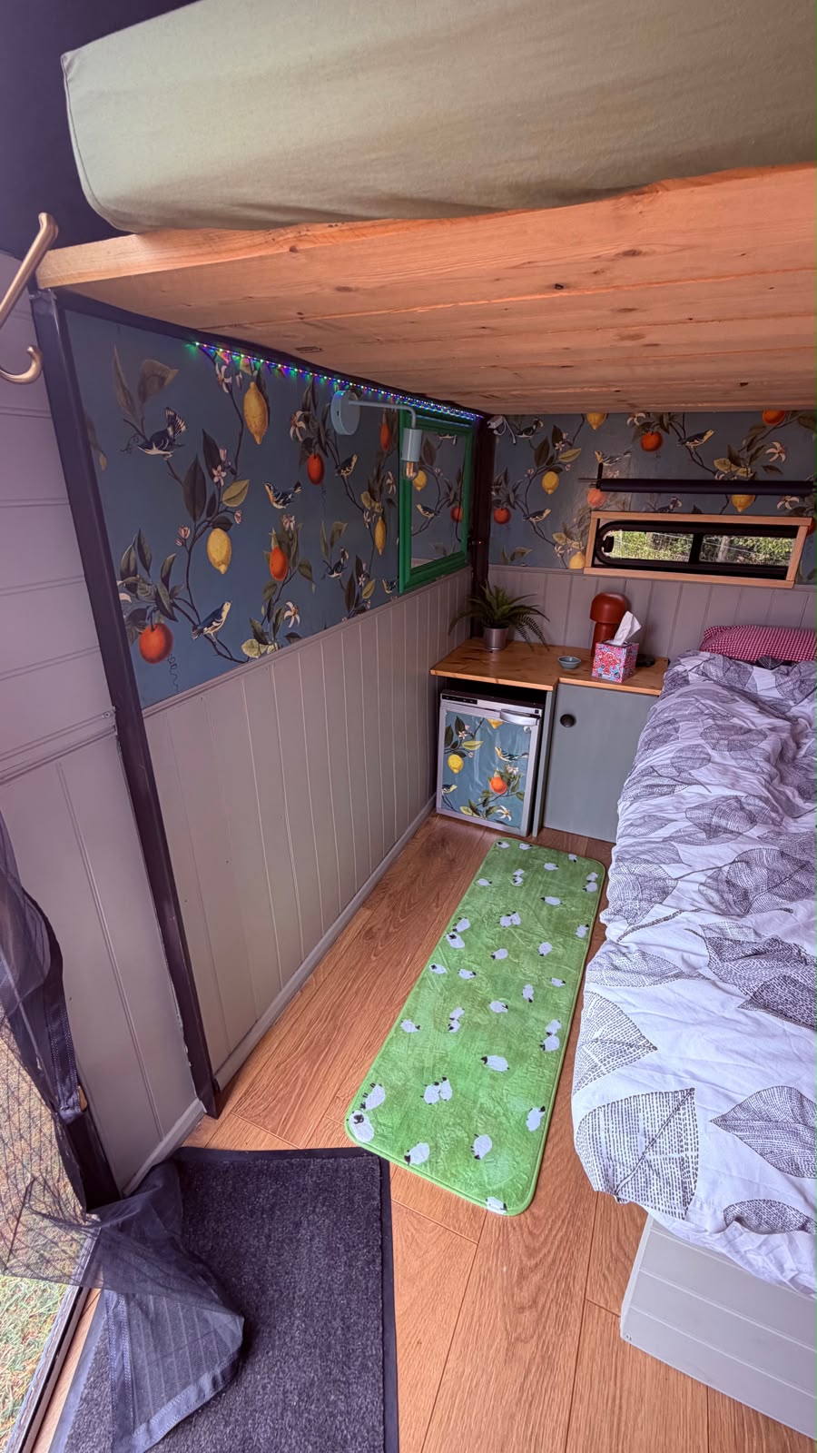 Inside the converted horse box, with a bed, bunk and lemon wallpaper