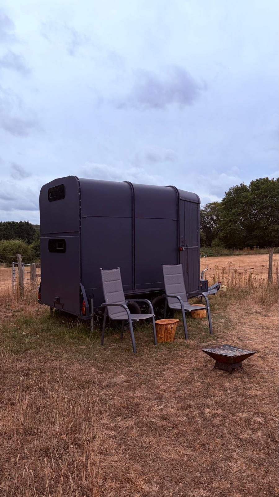 Converted horse box with two chairs and a fire pit on the grass