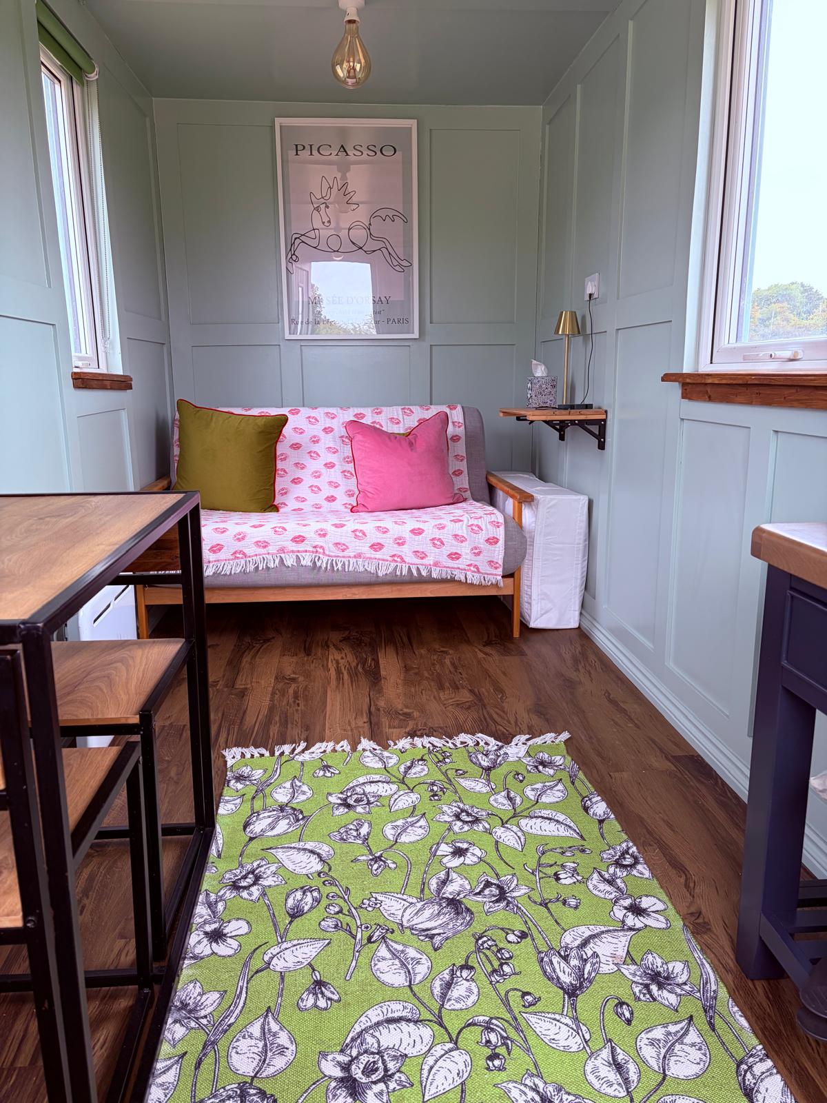 Interior of the small shepherd’s hut with sofa, floral rug and countryside views